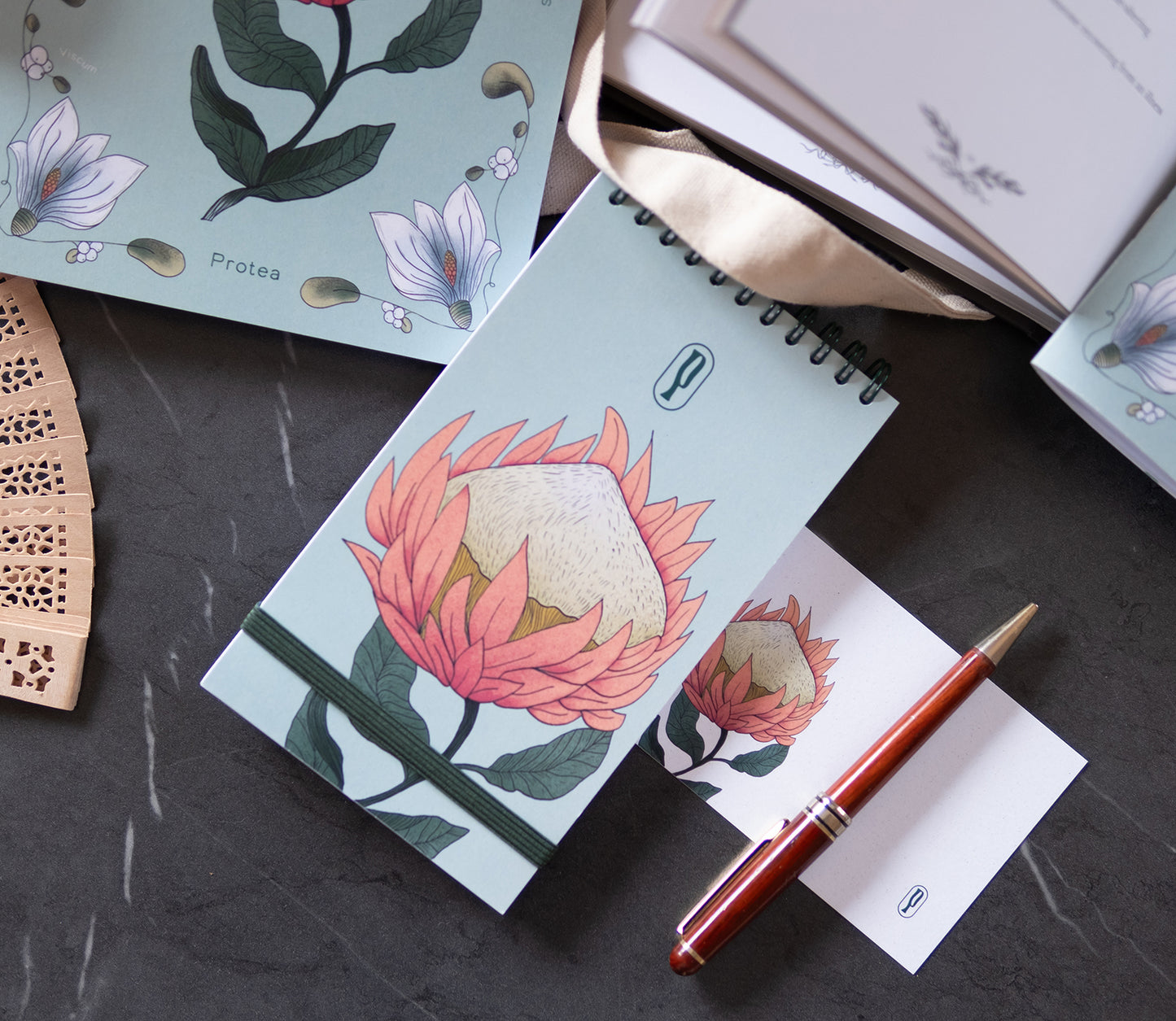 Colombo Protea di Piperita Paper: taccuino tascabile 10x17 cm, pagine bianche, copertina con stampa floreale e spirale, perfetto per appunti e idee creative.