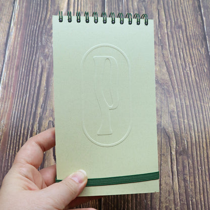 Colombo di Piperita Paper: taccuino tascabile 10x17 cm, pagine bianche, copertina verde e sabbia con rilievo e spirale, perfetto per appunti e idee.